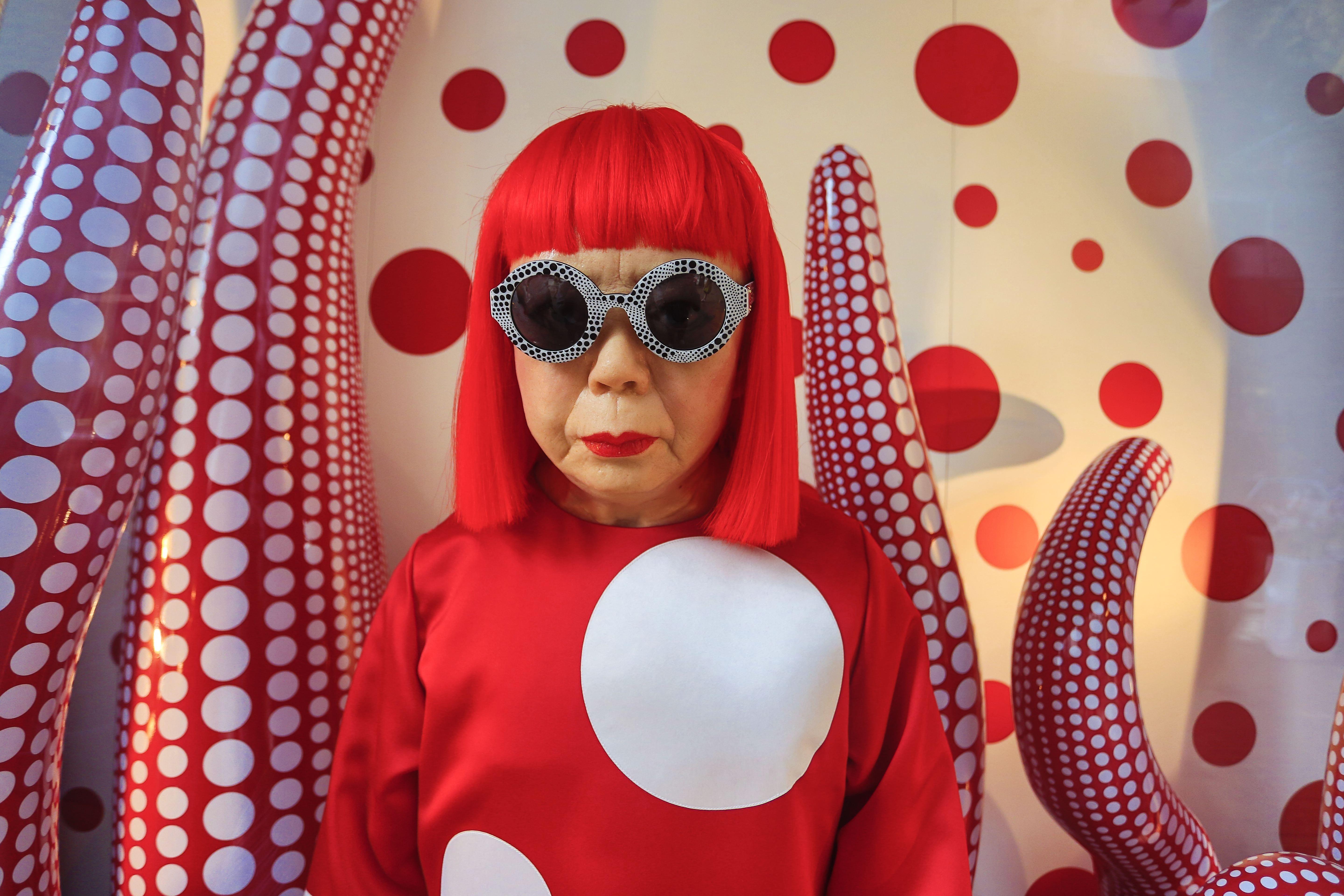 Jajoi Kusama sa crvenom perikom na glavi obučena u crvenom sa belim tufnama