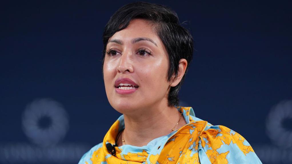 Žena u majici žuto plavih šara, govori na konferenciji, ima kratku crnu kosu