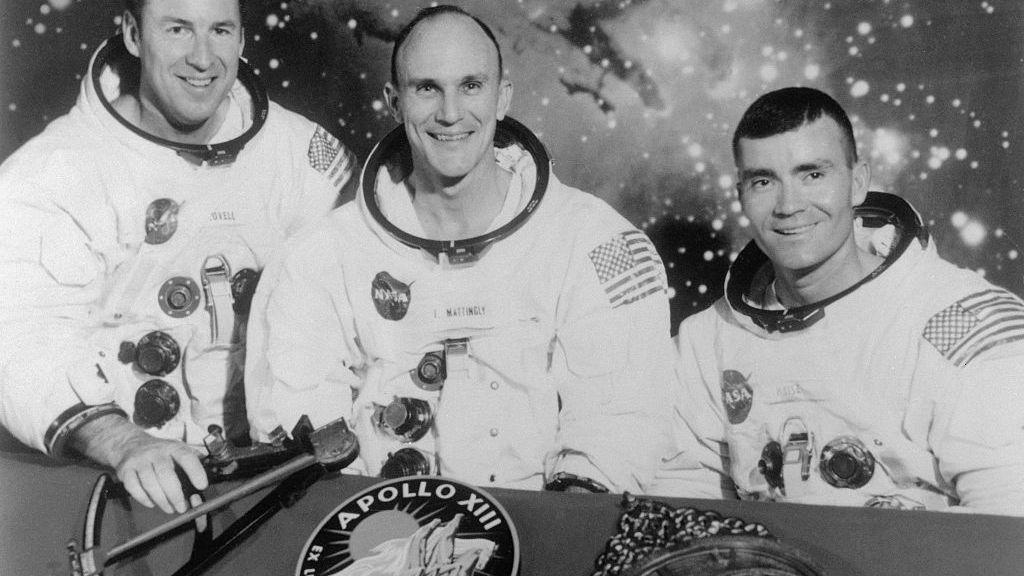 Crno-bela fotografija tri astronauta u svemirskim odelima koji se smeše iza stola;  jedan od njih drži sekstant