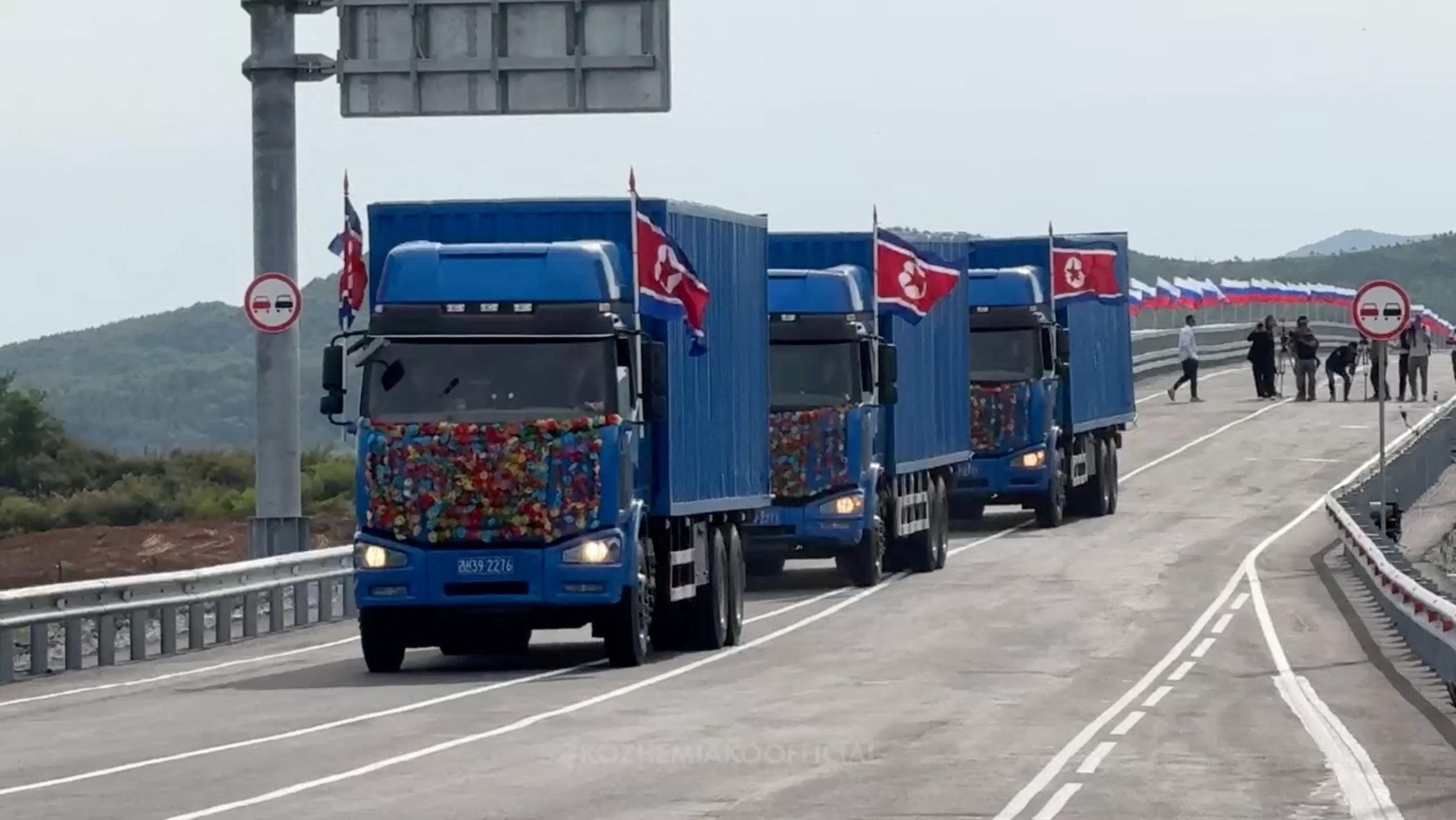 Tri plava kamiona sa severnokorejskim zastavama na mostu i ruske zastave koje se vijore sa bandera