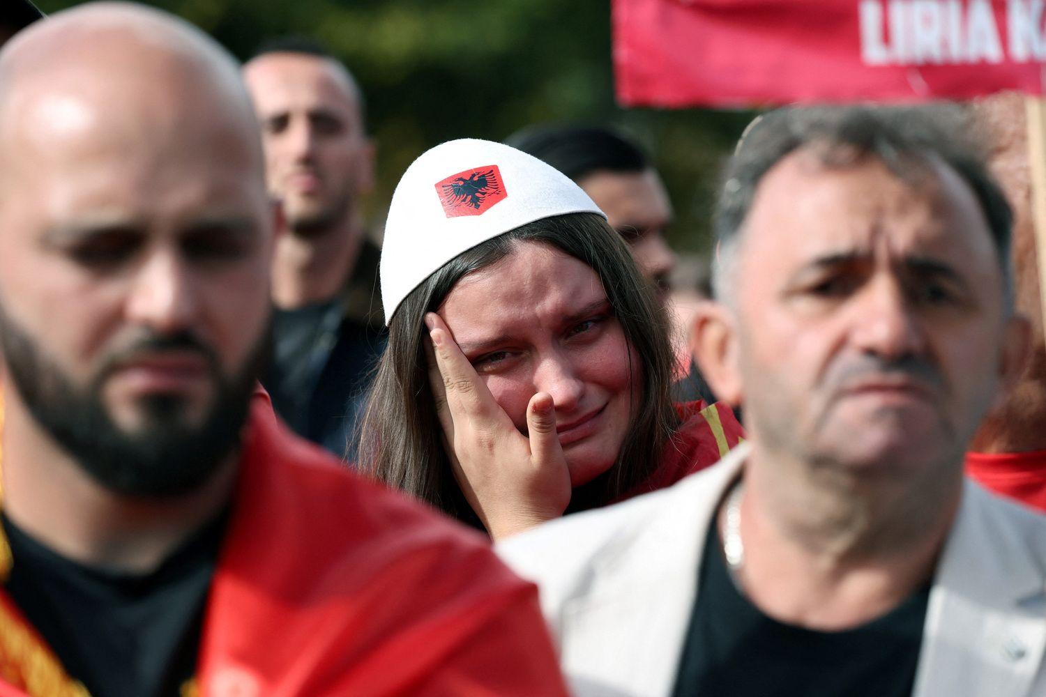 Devojka briše suze sa lica sa belom kapom na glavi sa albanskom zastavom