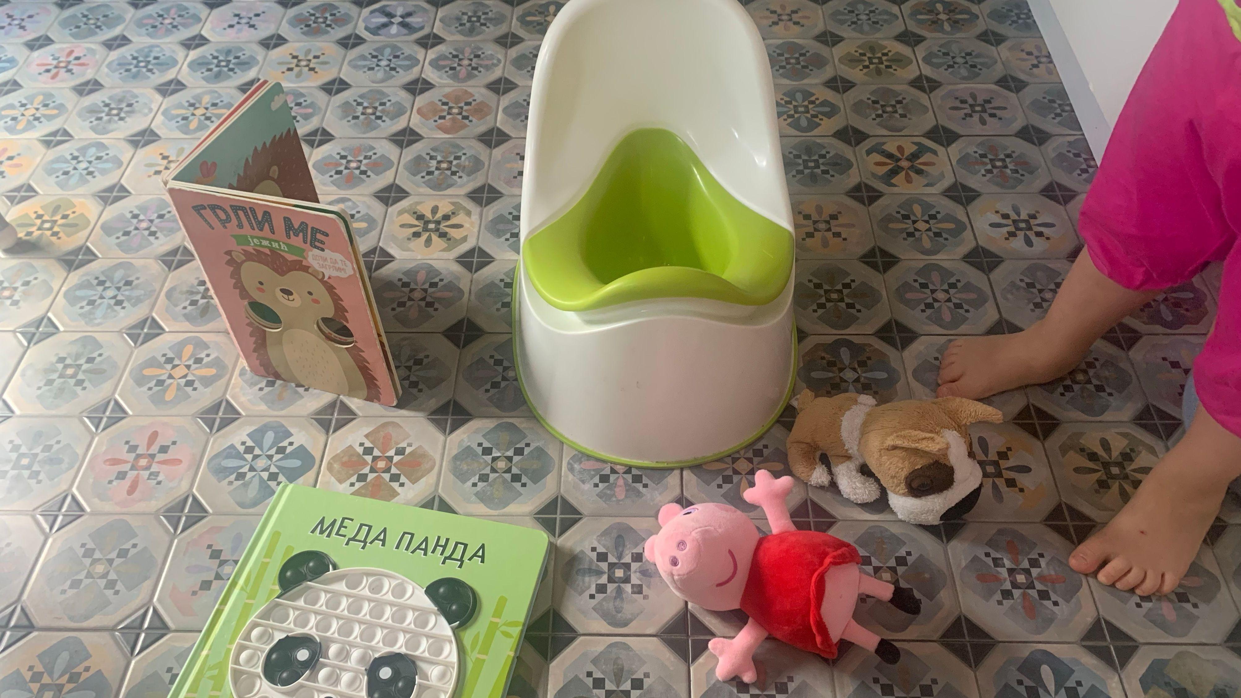 zeleno bela plastična noša na šarenim pločicama, pored je malo dete, igračke na podu 