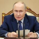 Putin sedi za stolom ispred mikrofona, a u rukama drži beleške