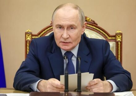 Putin sedi za stolom ispred mikrofona, a u rukama drži beleške