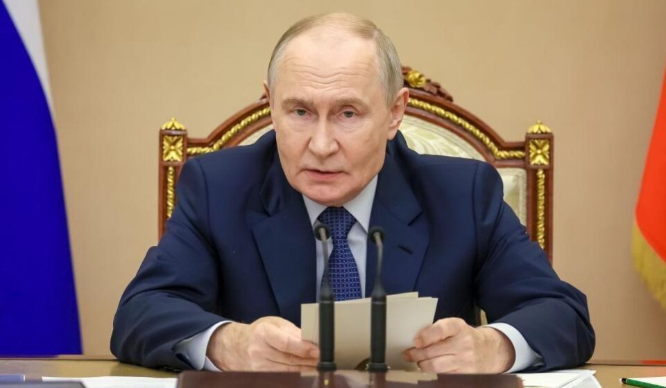 Putin sedi za stolom ispred mikrofona, a u rukama drži beleške