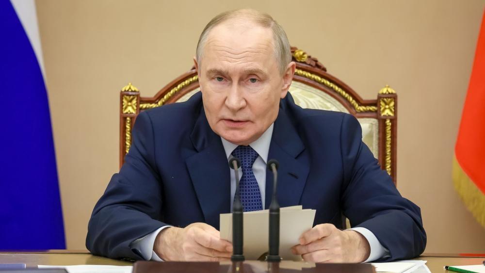 Putin sedi za stolom ispred mikrofona, a u rukama drži beleške