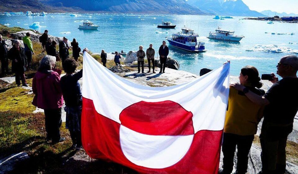 ljudi drže zastavu Grenlanda na obali ostrva