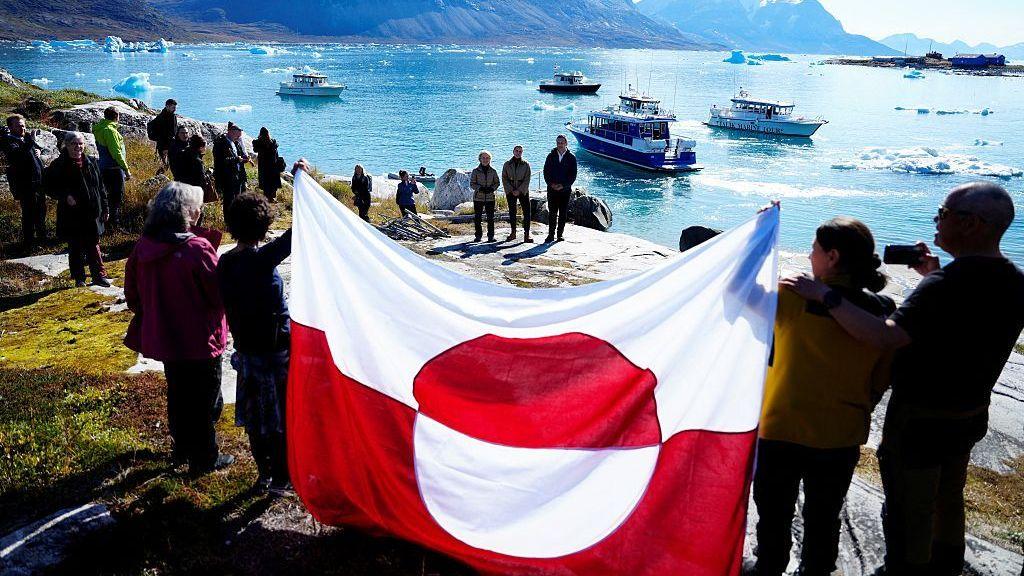 ljudi drže zastavu Grenlanda na obali ostrva