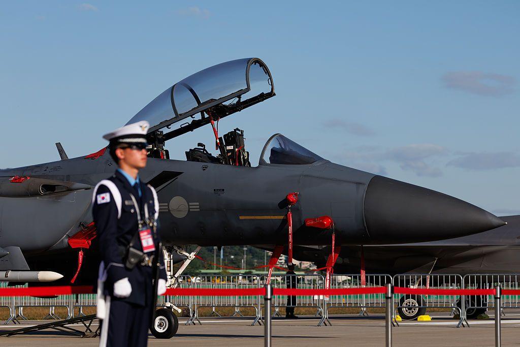 Borbeni avion južnokorejskog vazdušnih snaga izložen na aerodromu, sa otvorenim pilotskom kabinom, dok uniformisani stražar stoji u prvom planu 
