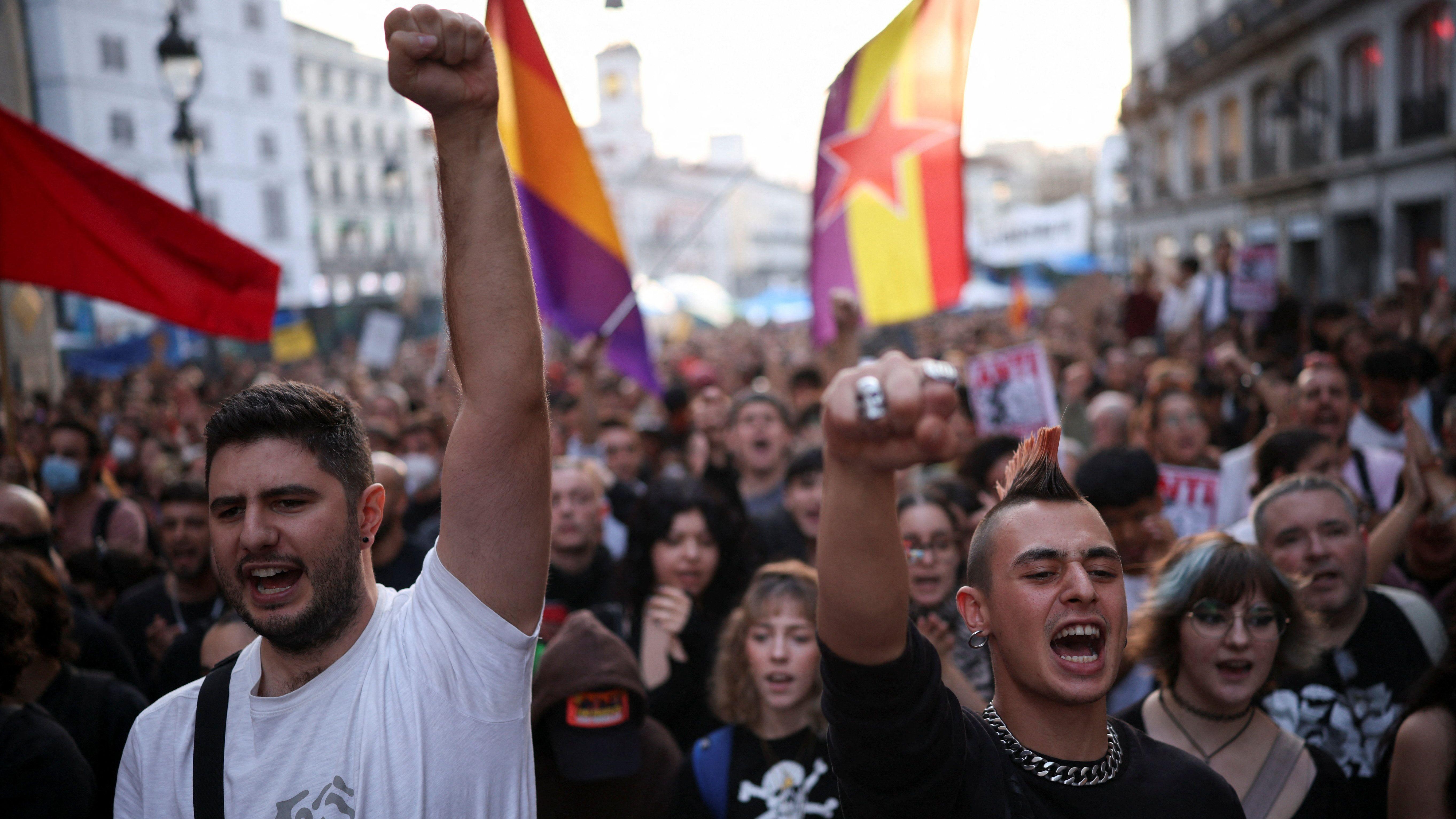Dva muškarca sa dignutim pesnicama uzvikuju, iza njih masa ljudi i zastave sa petokrakom