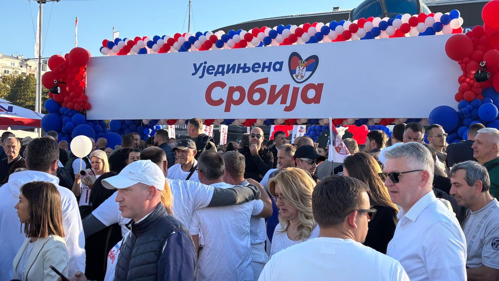 Ljudi ispred štanda sa balonima u bojama srpske zastave, ispod njih piše Ujedinjena Srbija