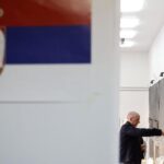 Čovek ubacuje glasački listić u kutiju u krupnom planu zastava Srbije