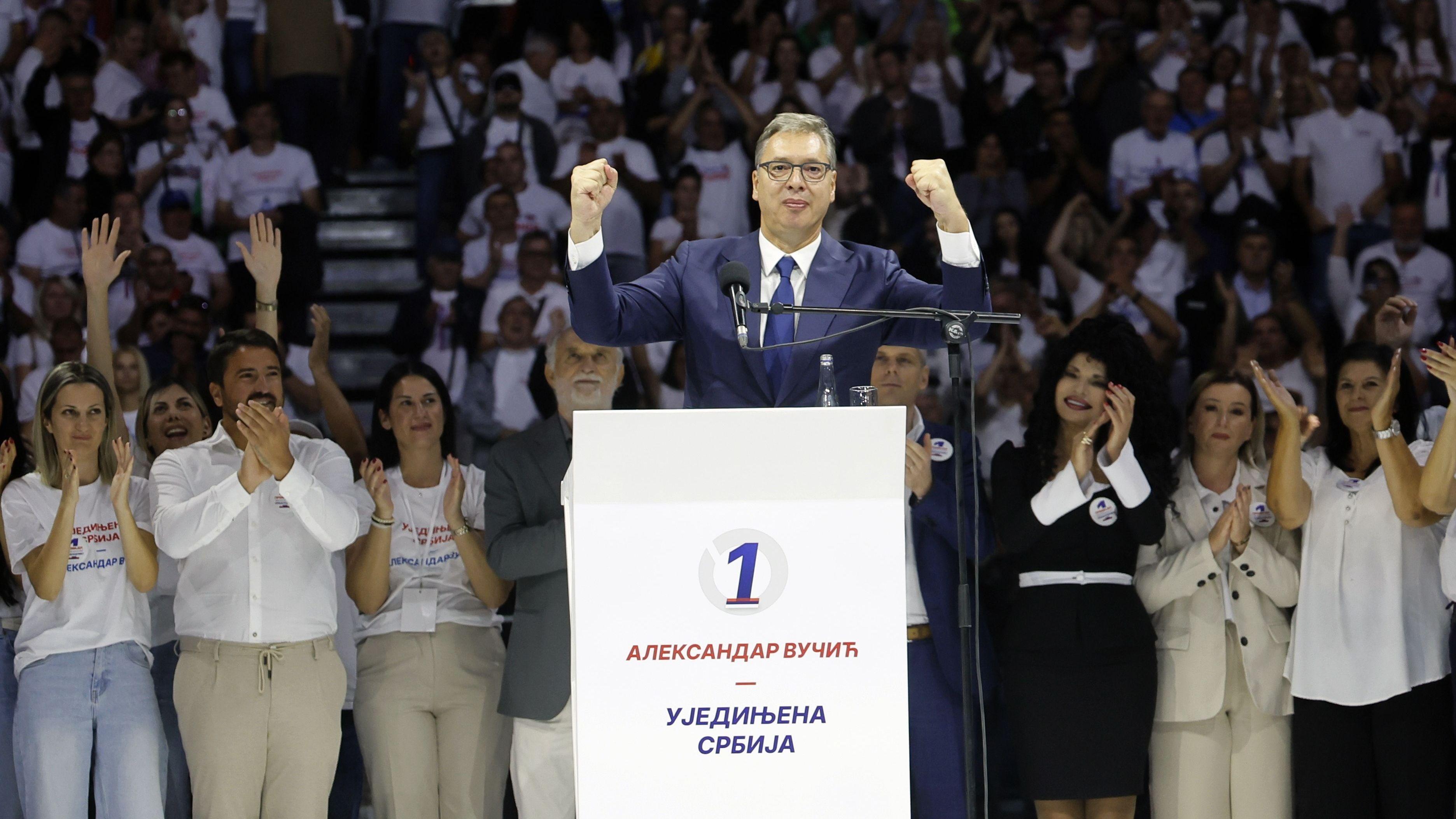 Aleksandar VUčić u plavom odelu i svetloj košulji podiže ruke u vazduh, stoji za govornicom, oko njega je mnogo ljudi