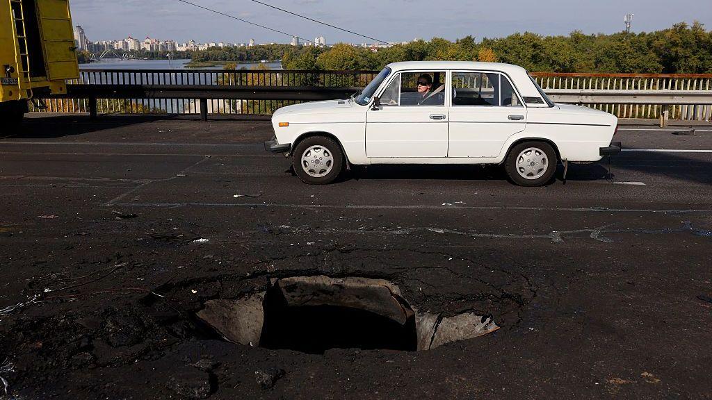 Beli automobil prolazi pored rupe na betonskom kolovozu mosta Pivnični, koji je pogođen ruskim dronom.