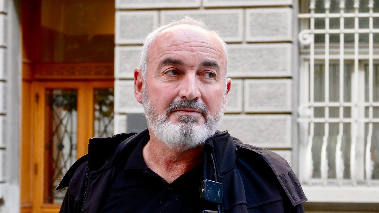 Milovan Milivojević, sede kose i brade, gleda u stranu, u crnoj je jakni i majici, iza njega je zgrada, otac poginulog mladića u fabrici u lučanima, namenska u lučanima