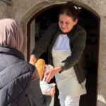 Žena okrenuta leđima uzima kesu od druge žene u kojoj je hleb
