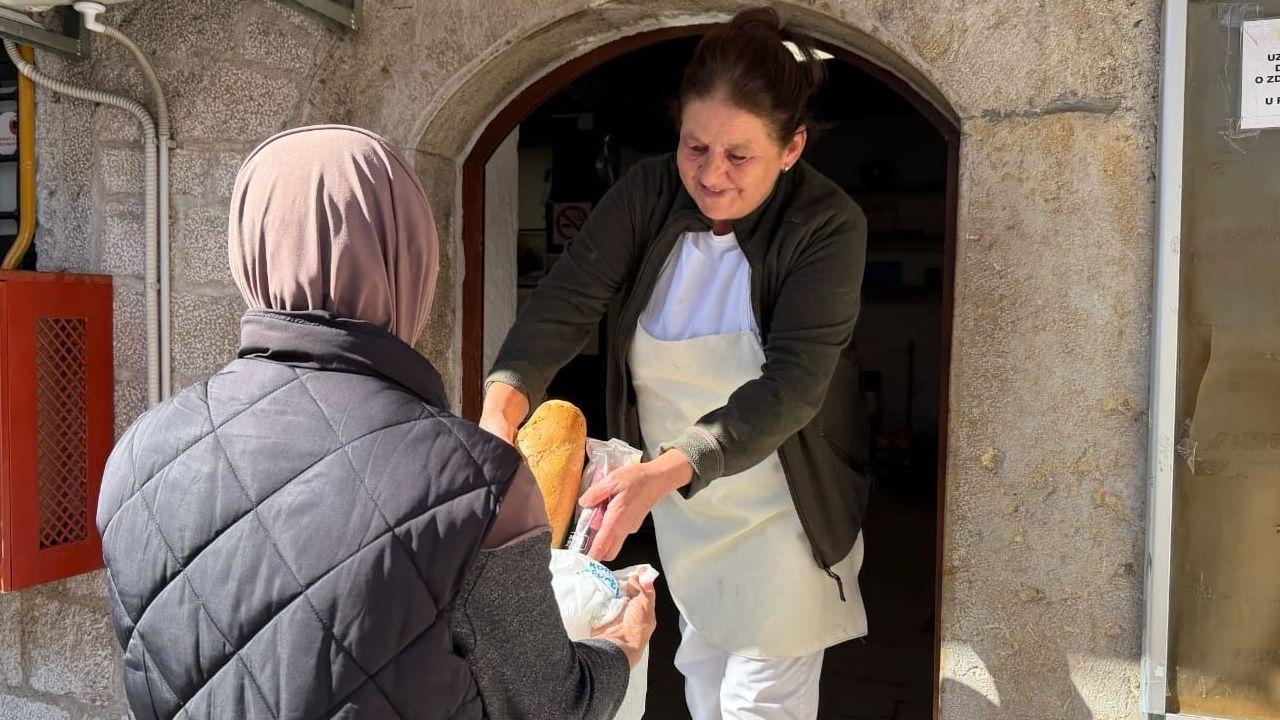 Žena okrenuta leđima uzima kesu od druge žene u kojoj je hleb